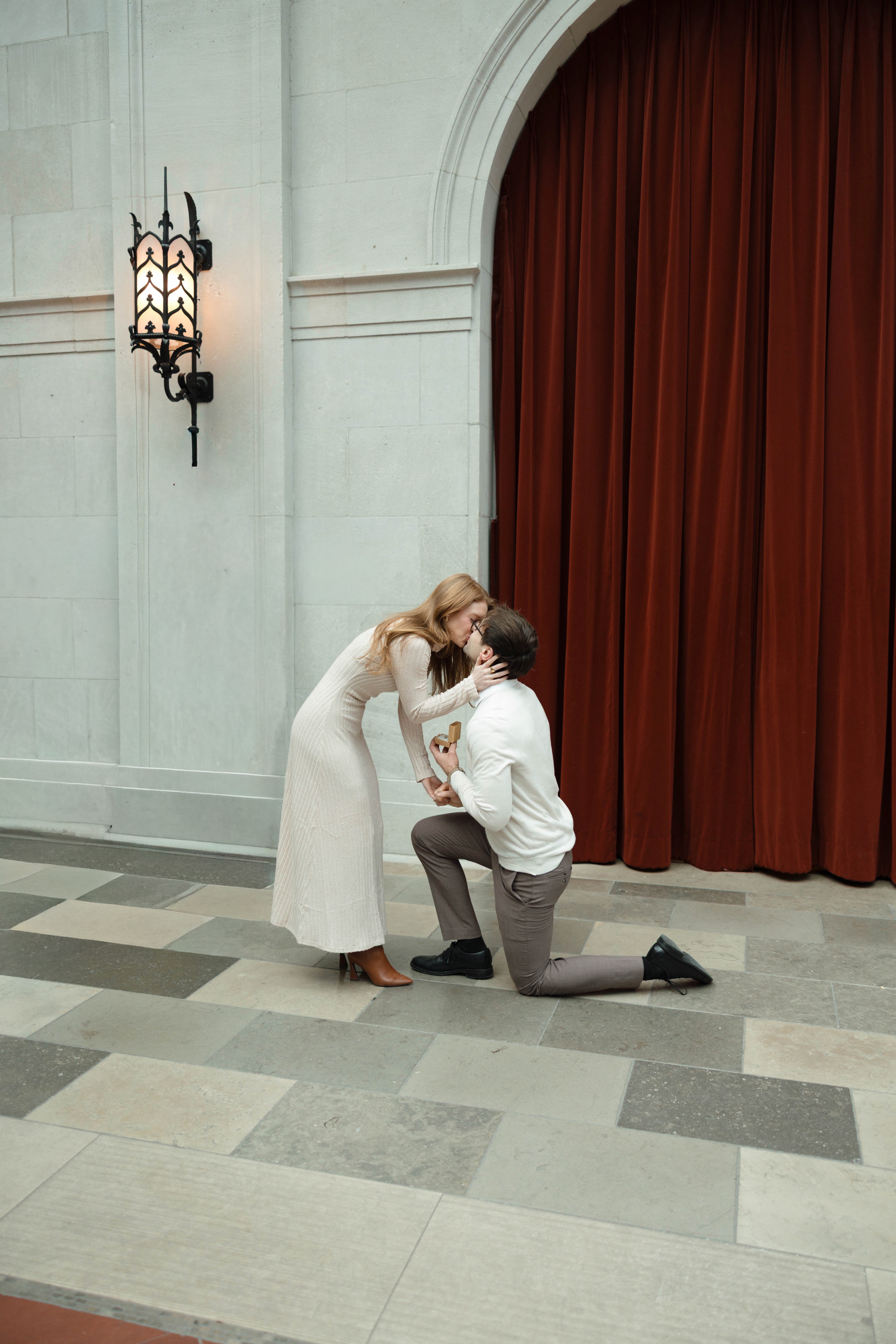 Cody down on one knee proposing to Katrina in front of the red velvet curtains